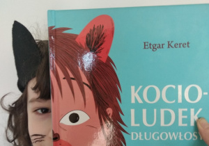 Kontanty Robert: Na zdjęciu widzimy twarz chłopca z wąsami i sterczącym uchem. Połowę twarzy zastąpiono okładką książki Etgara Kereta „Kocio- Ludek długowłosy”.